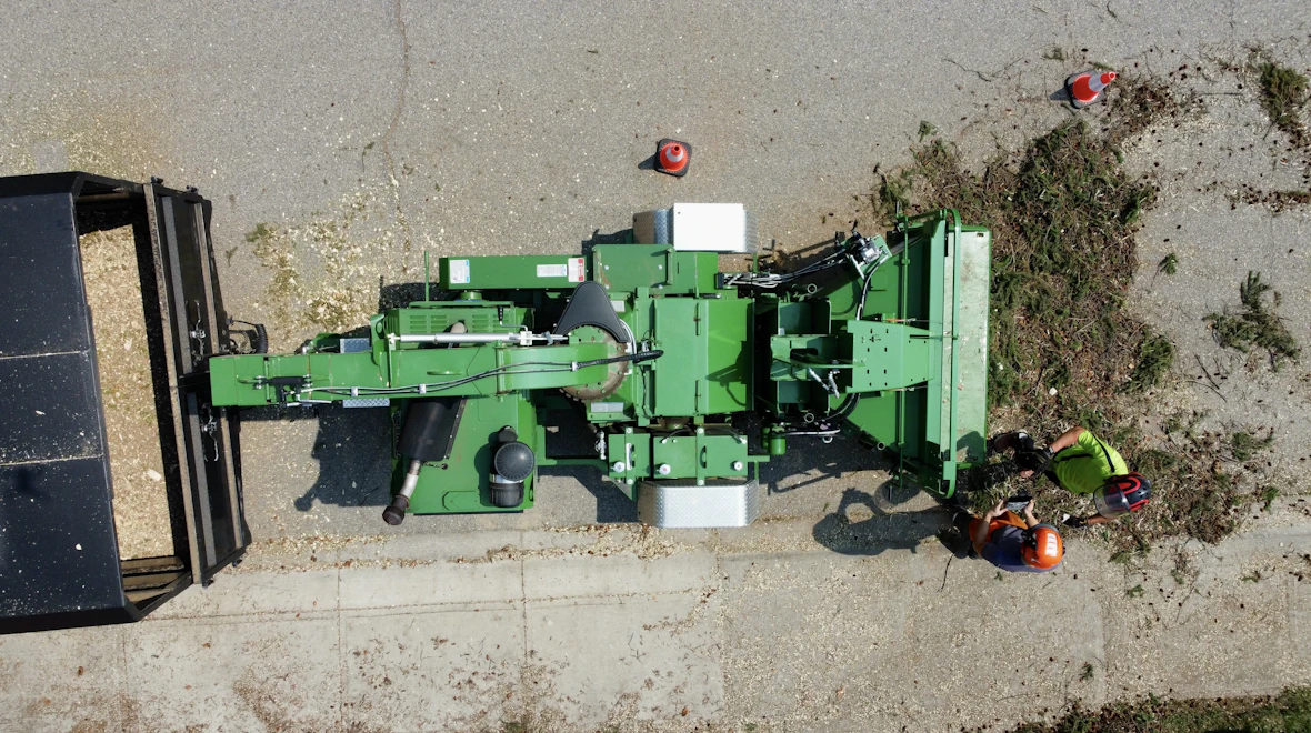 Two workers feeding storm-broken limbs into a drum chipper parked at the curb